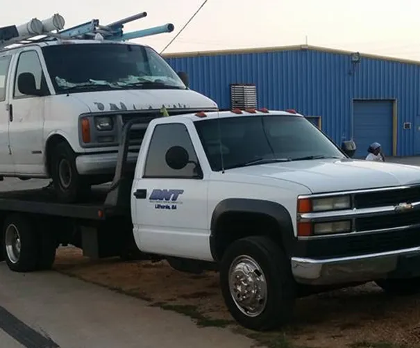 White flatbed tow truck hauling a white van.